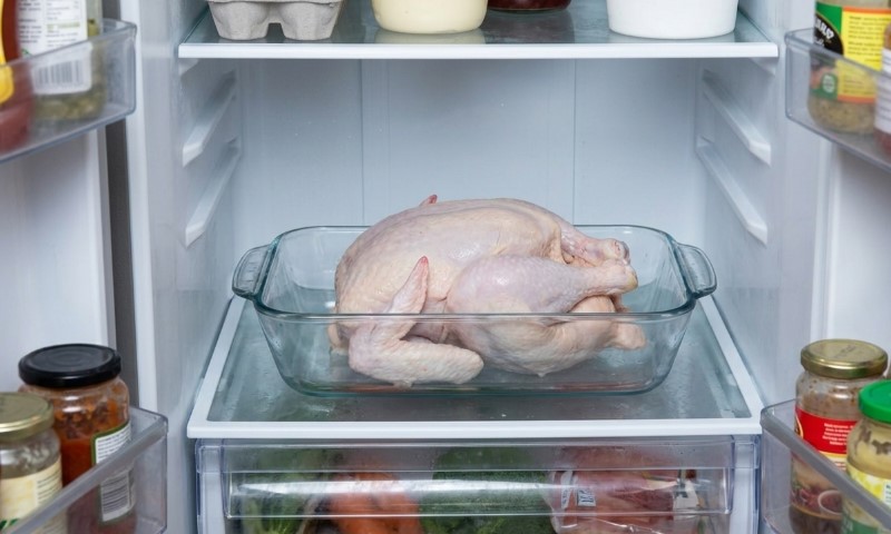 A raw whole chicken sits in a glass baking dish on a refrigerator shelf
