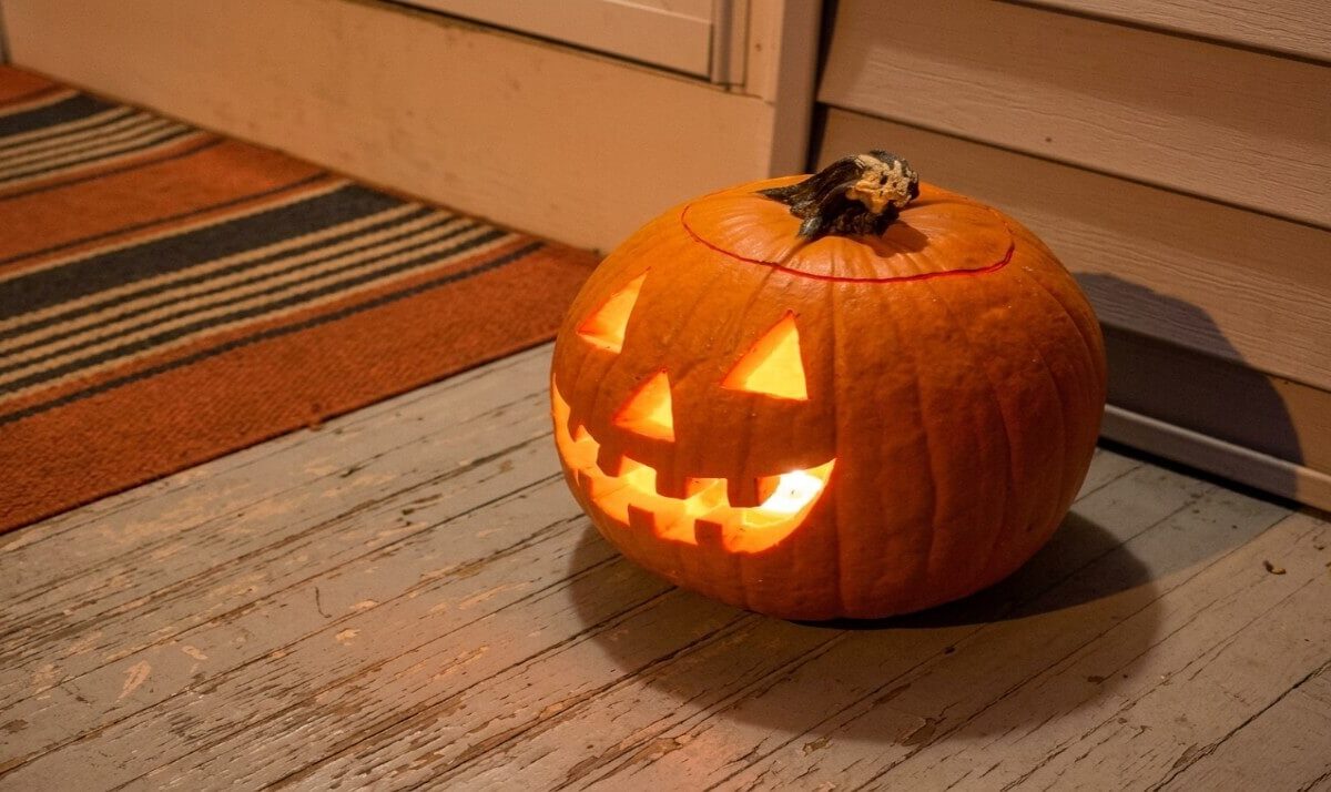 A carved Halloween pumpkin glows with a crooked, toothy grin on a weathered porch