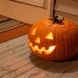 A carved Halloween pumpkin glows with a crooked, toothy grin on a weathered porch