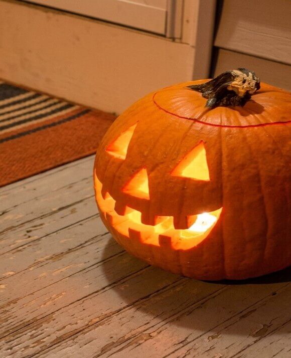 A carved Halloween pumpkin glows with a crooked, toothy grin on a weathered porch