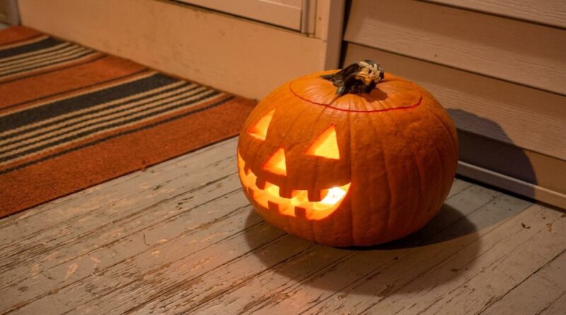 A carved Halloween pumpkin glows with a crooked, toothy grin on a weathered porch