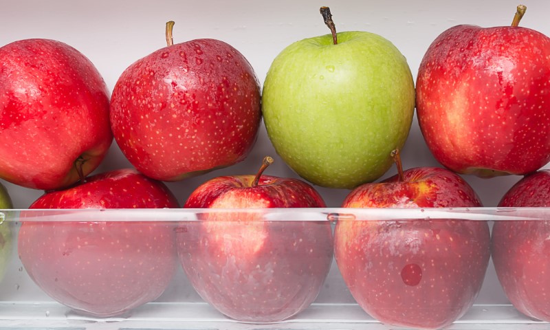Red and green apples are stacked in a clear glass bowl