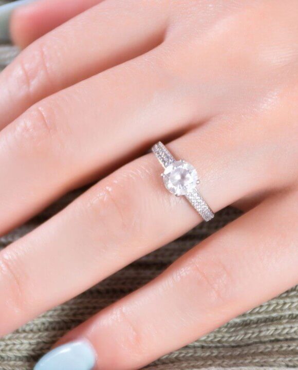 A hand with pale blue and glitter-polished nails wears a sparkling diamond engagement ring