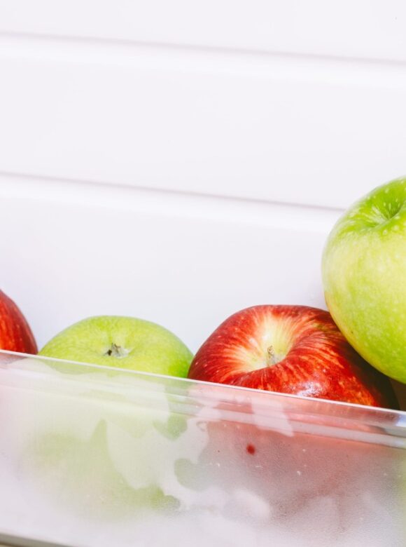A clear refrigerator drawer holds red and green apples, including a bright green apple in front