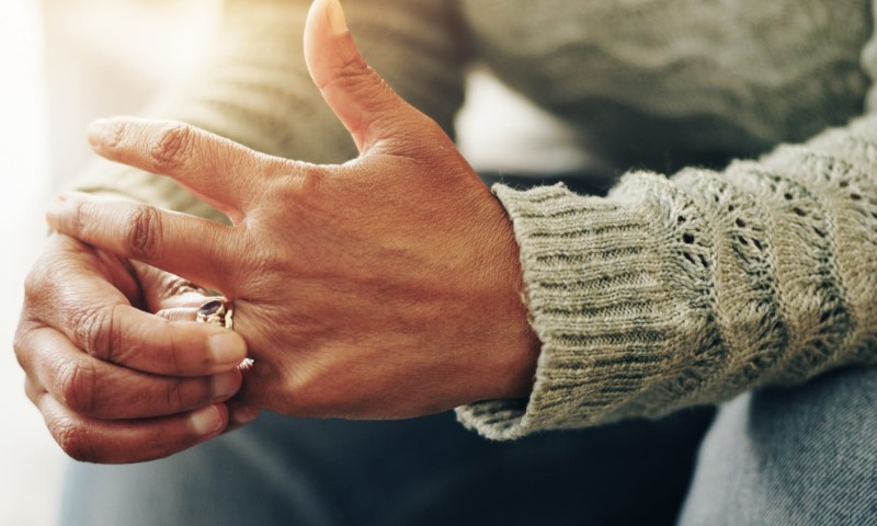 Close-up of two hands in knitted sleeves, one holding a small ring near the other’s fingers