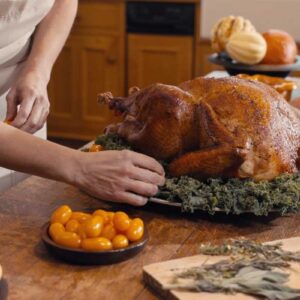 Roasted Thanksgiving turkey being prepared on a festive table with seasonal vegetables and herbs.