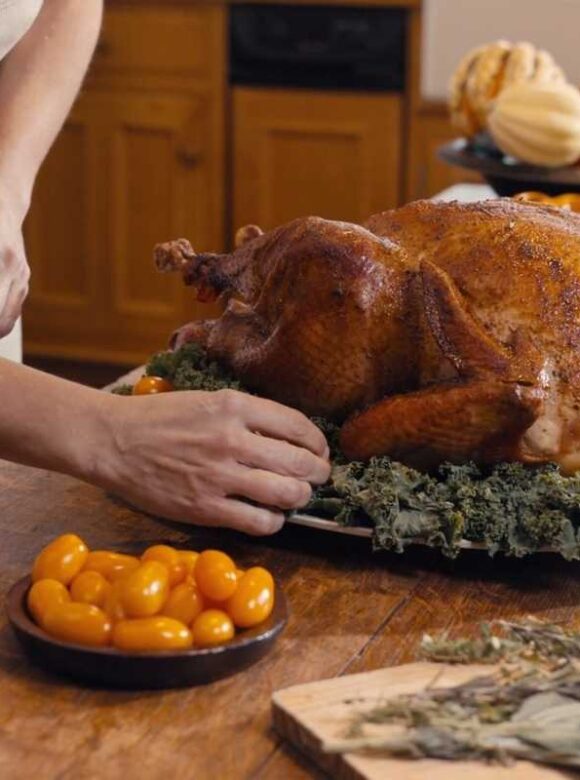 Roasted Thanksgiving turkey being prepared on a festive table with seasonal vegetables and herbs.