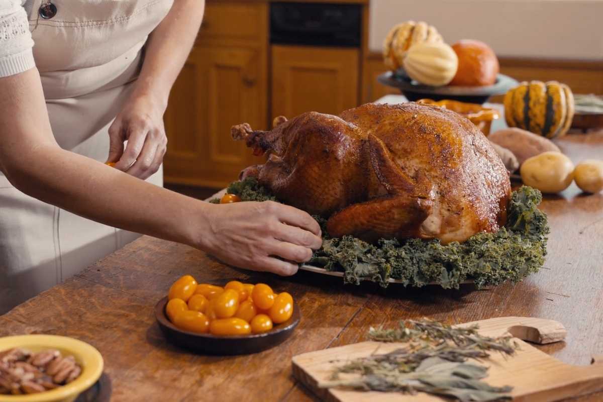 Roasted Thanksgiving turkey being prepared on a festive table with seasonal vegetables and herbs.