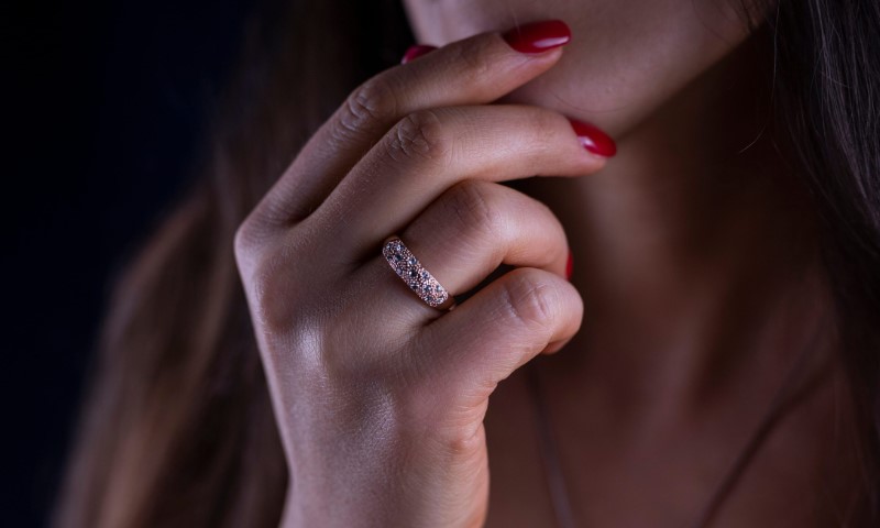 Close-up of a woman’s hand with glossy red nails and a sparkling ring held near her lips