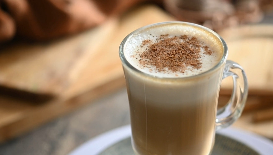 A pumpkin spice latte topped with foam and cinnamon in a glass mug.